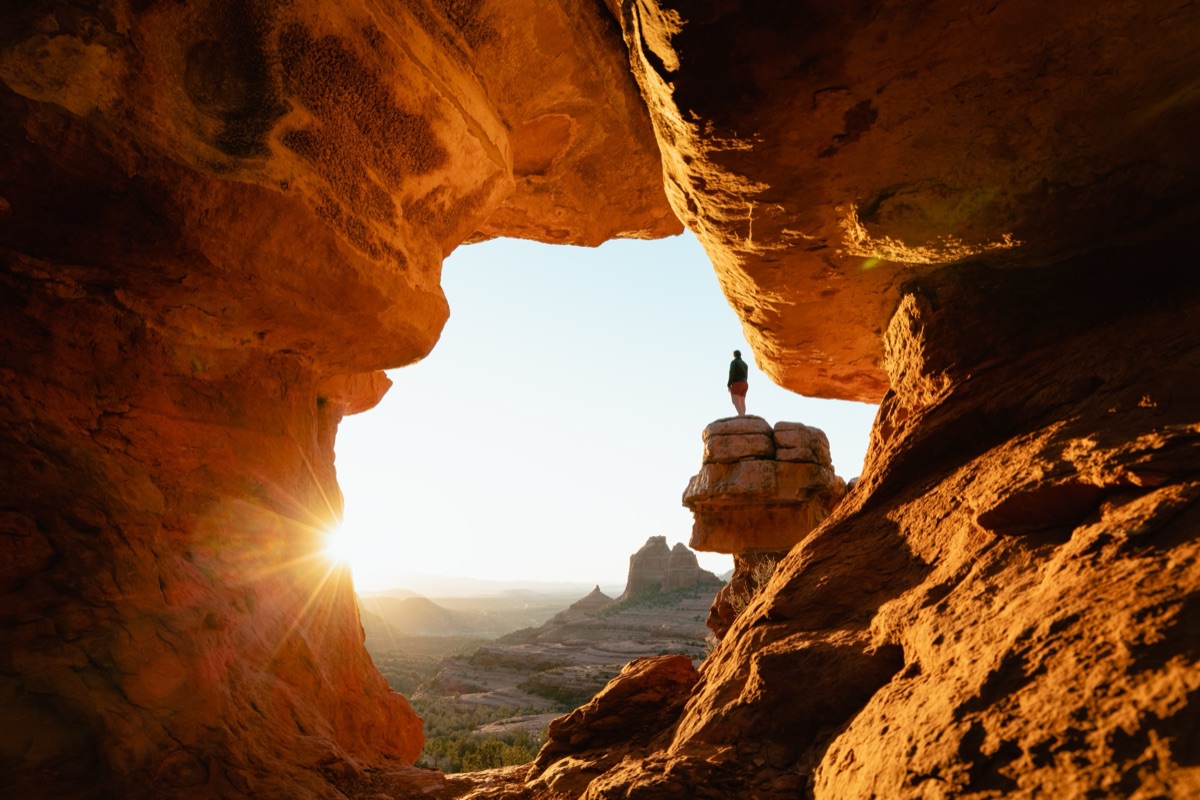A person standing at a clifftop opening, looking out towards the sunrise